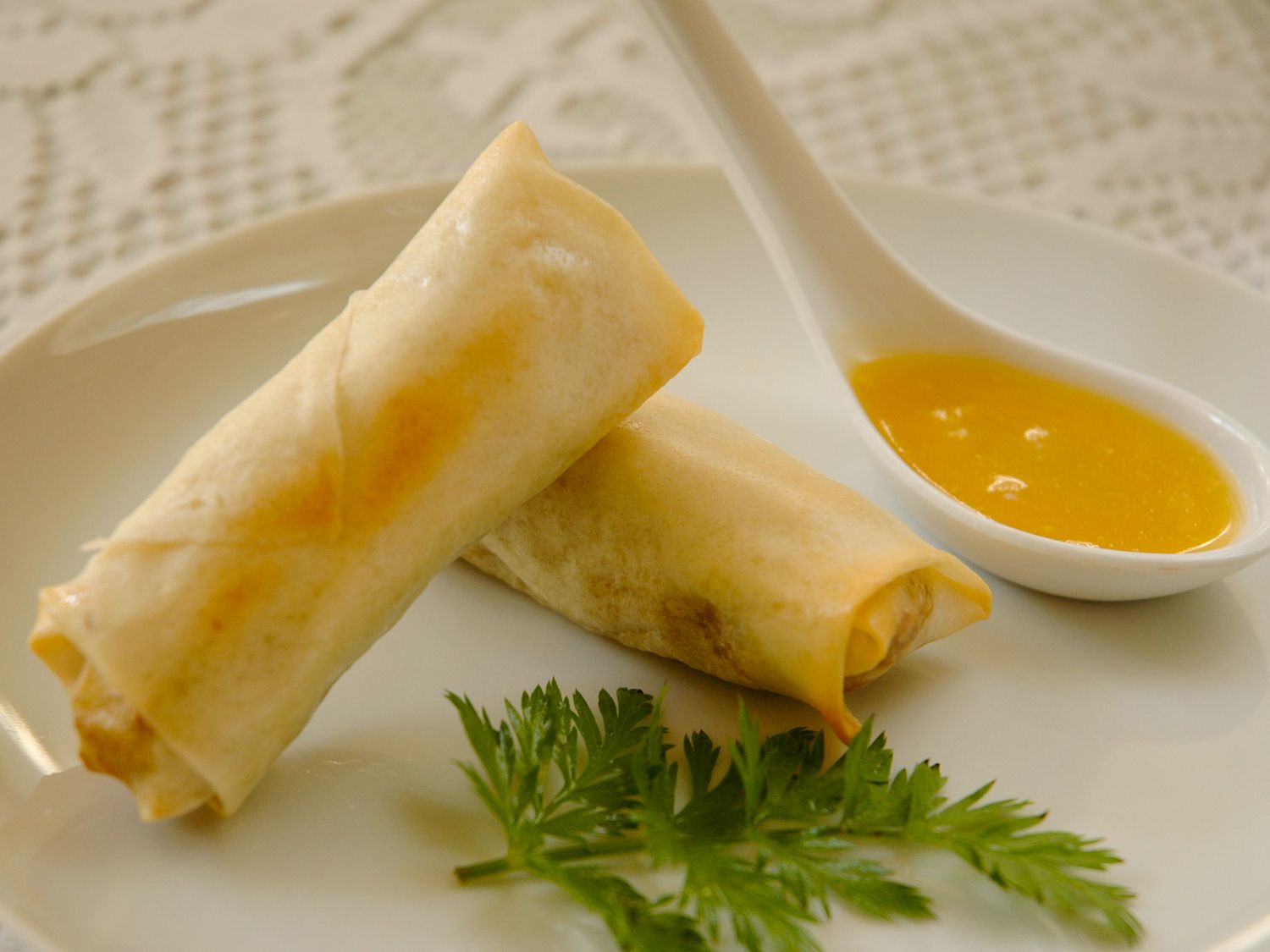 close up view of Baked Pork Spring Rolls with fresh herbs and sauce in a spoon on a white plate