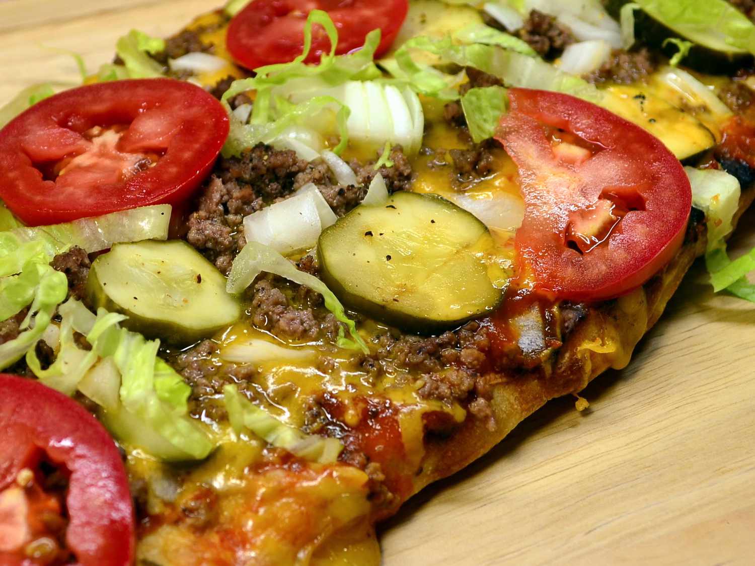 close up view of Cheeseburger Pizza on a wooden cutting board
