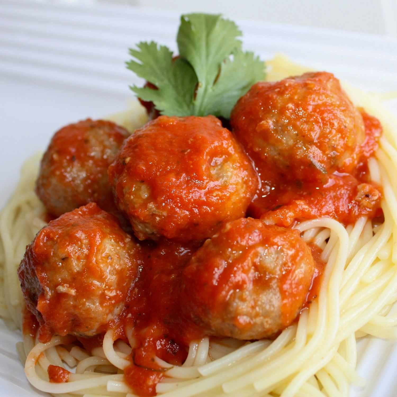 close up view of Meatballs with sauce over spaghetti on a white plate