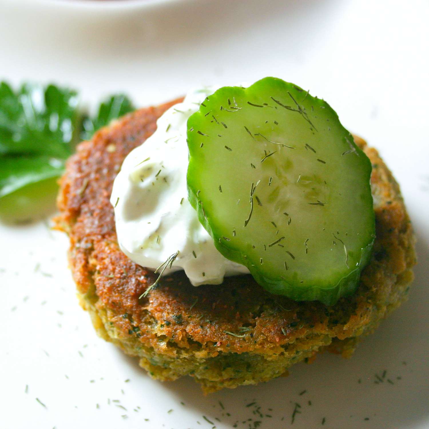 close up view of a Falafel with a slice of Cucumber and Sauce on a white plate