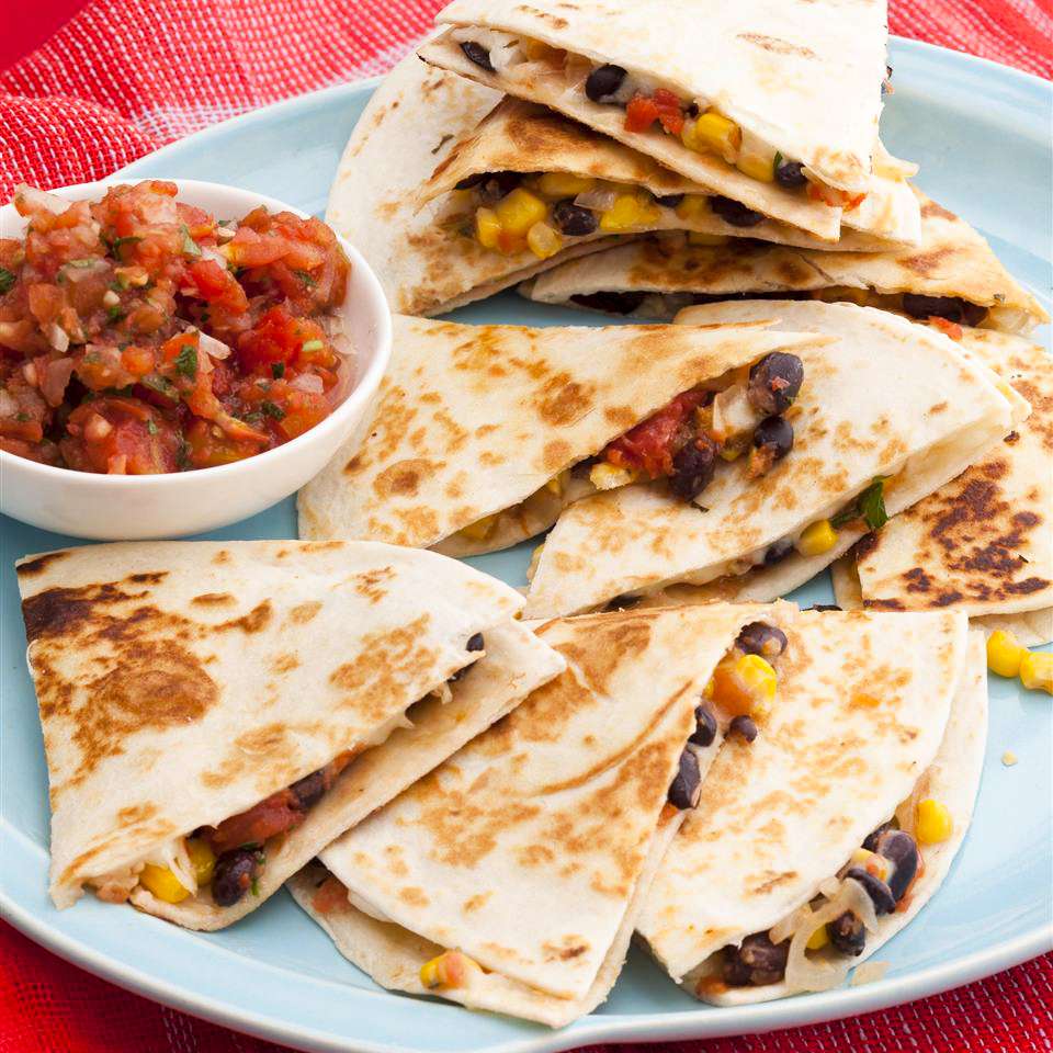 close up view of sliced Black Bean and Corn Quesadillas on a blue platter and salsa in a bowl