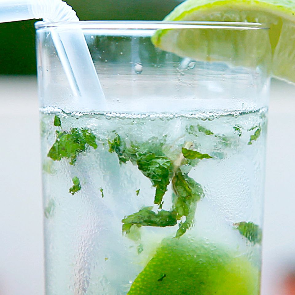 close up view of a Cuban Mojito in a glass with a straw, garnished with a lime wedge