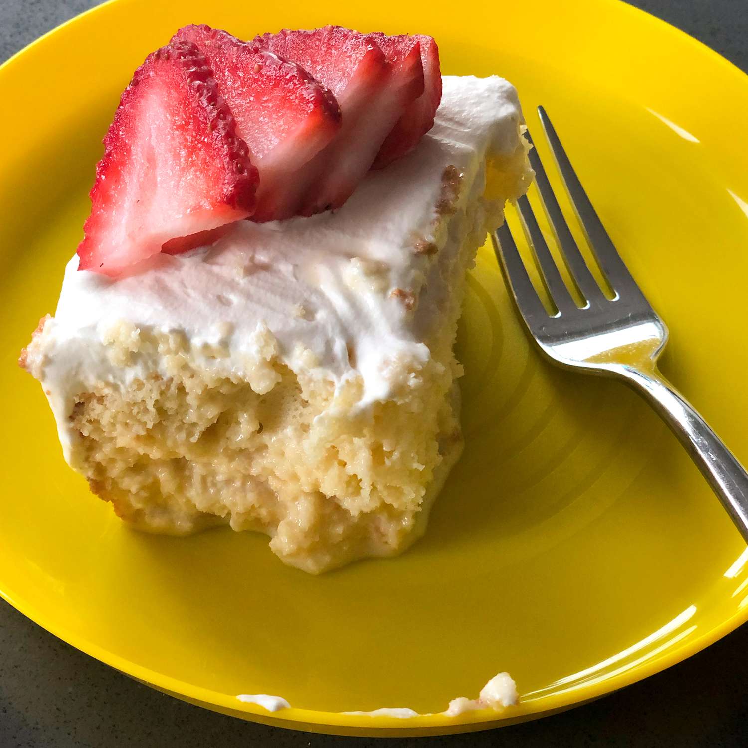 close up view of a slice of Tres Leches Cake garnished with sliced strawberries on a yellow plate with a fork