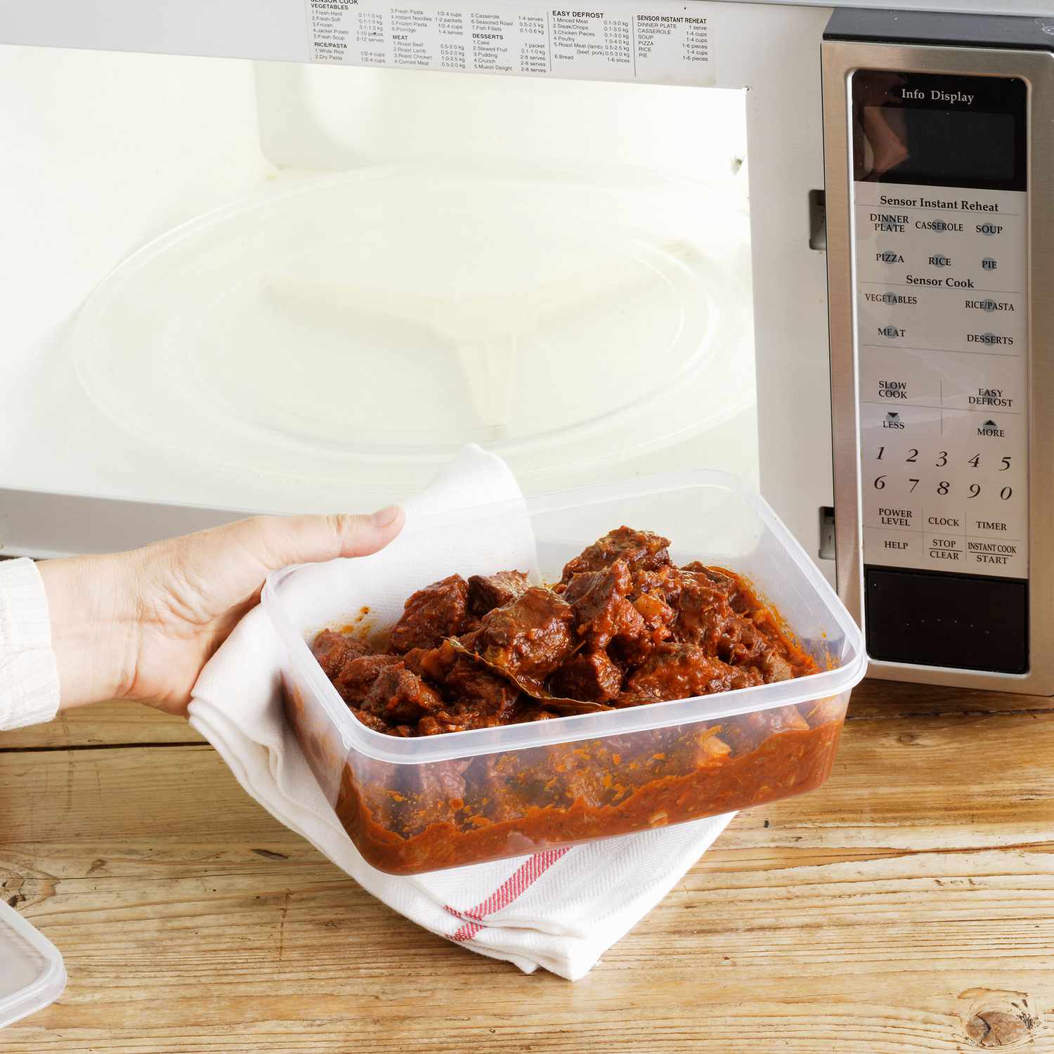 Woman heating leftovers in tupperware in microwave