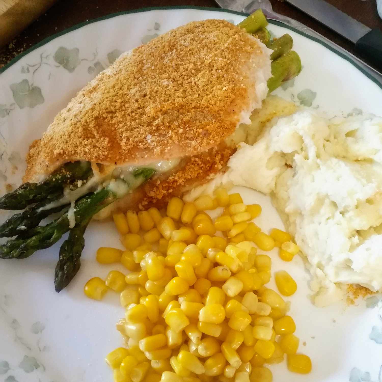 close up view of Asparagus and Mozzarella Stuffed Chicken Breasts, served with mashed potatoes and corn on a white plate