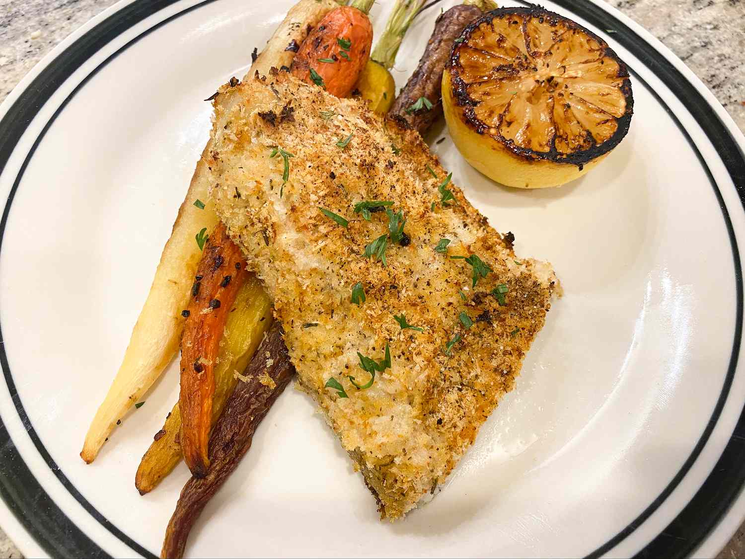 close up view of Barramundi With Lemon Basil Sauce over rainbow carrots garnished with a grilled lemon on a white plate