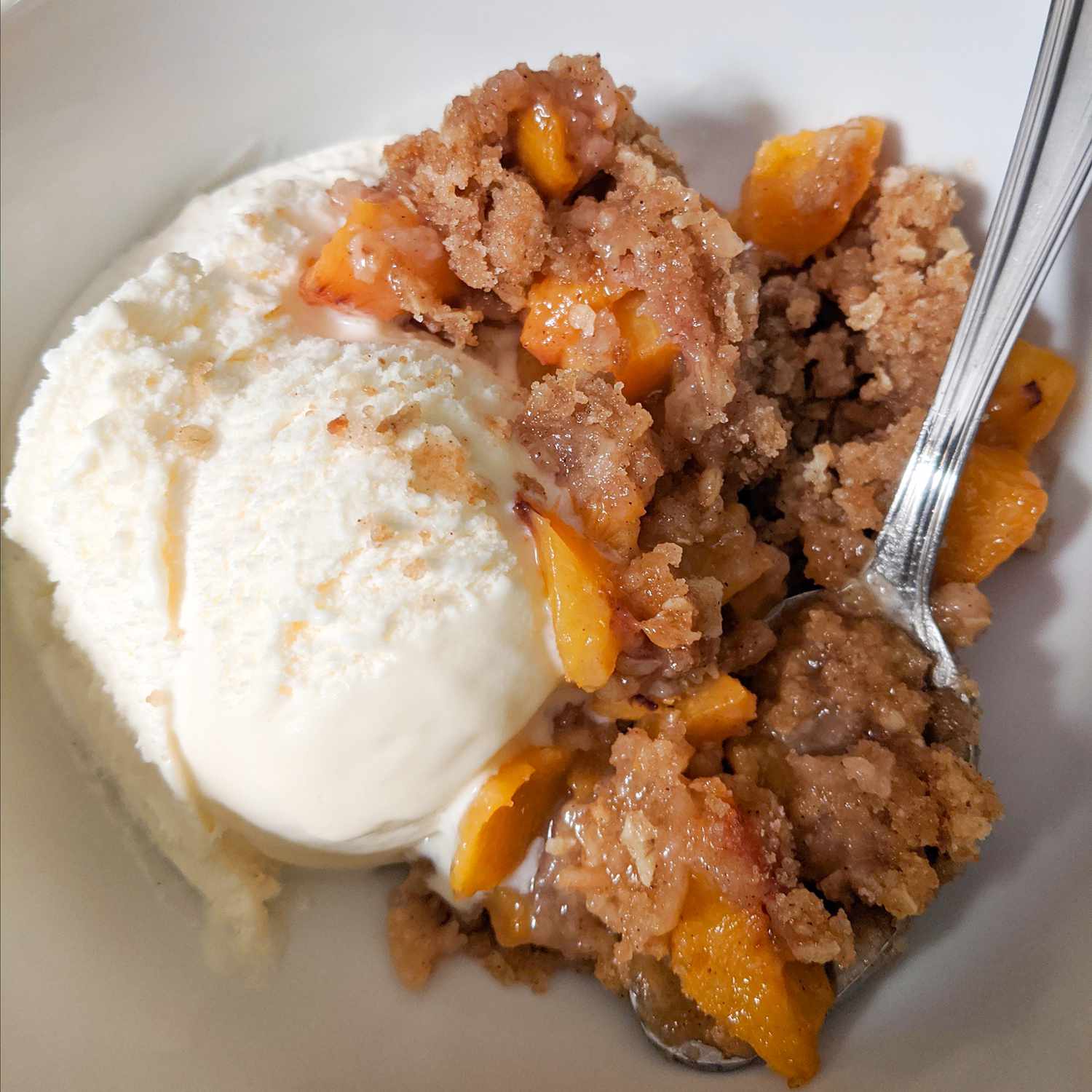 close up view of Juicy Peach Crisp served with ice cream in a bowl with a spoon