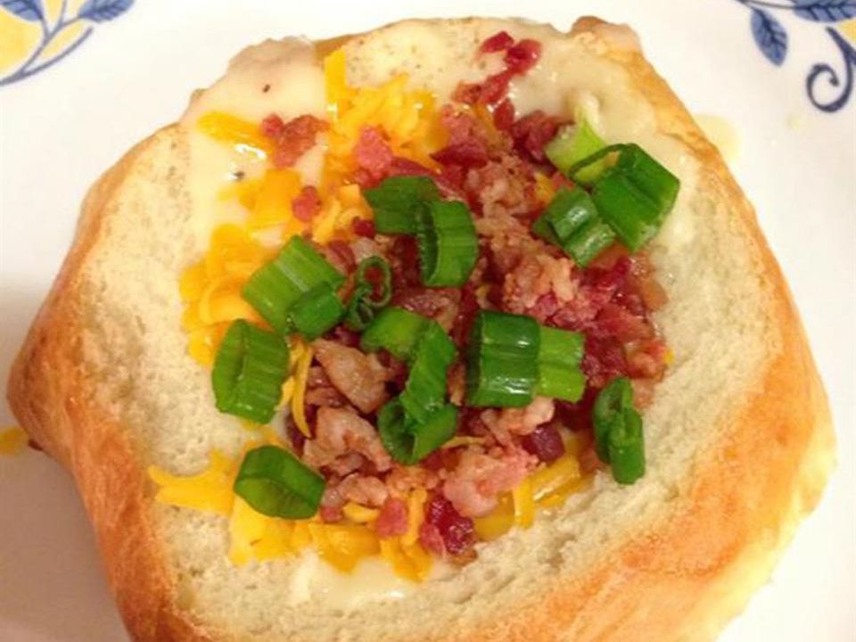 close up view of Potato Soup with Hash Browns in a bread bowl, garnished with bacon and green onions