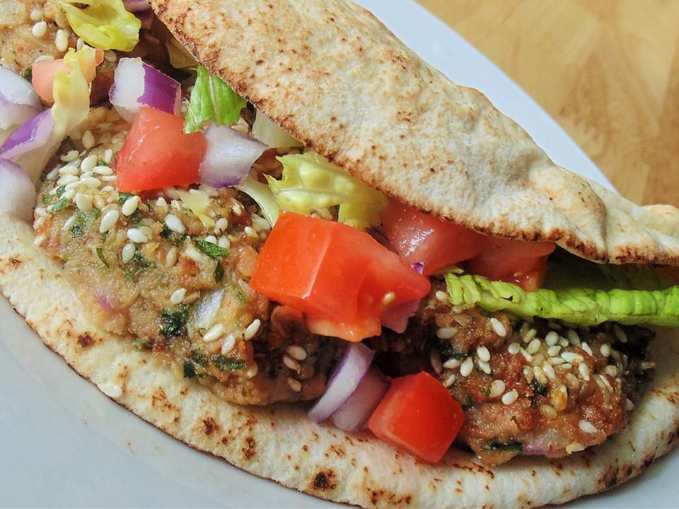 close up view of a Ta'ameya (Egyptian Falafel) sandwich with tomatoes, onions and lettuce on a white plate