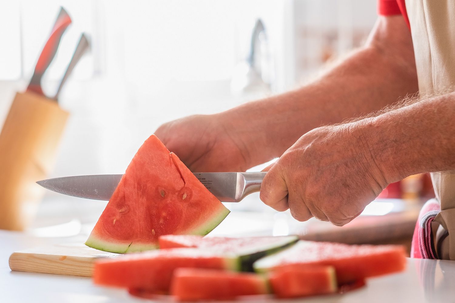 Caucasian senior man in home kitchen while cutting a ripe red wa
