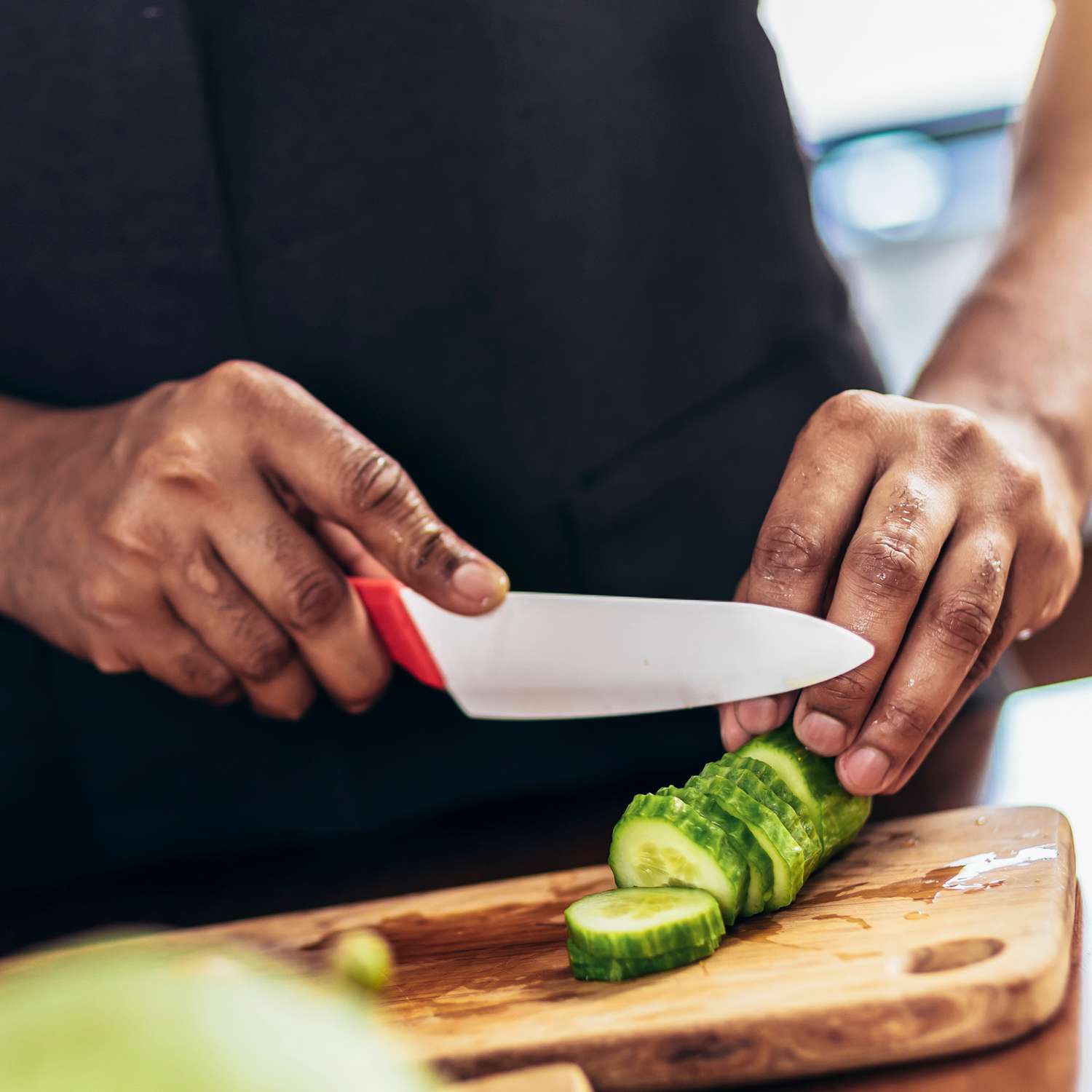 Close up shot of black man holding sharp knife cutting cucumber