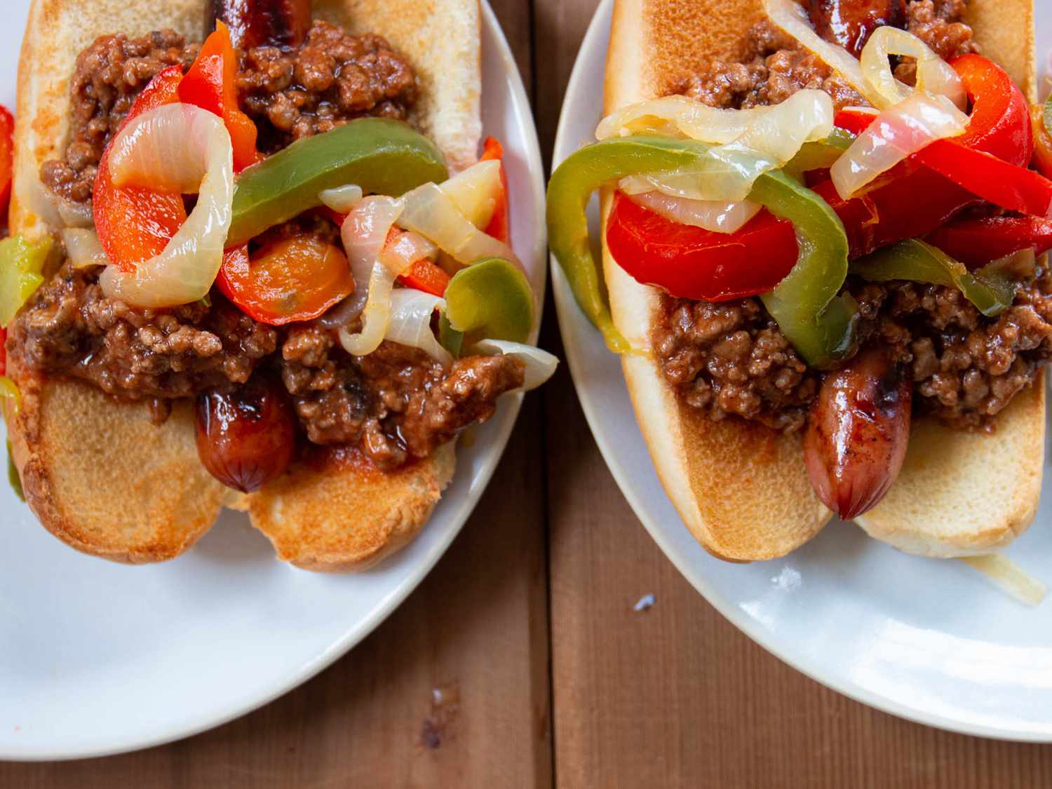 close up view of hot dogs with chili, peppers and onions on white plates