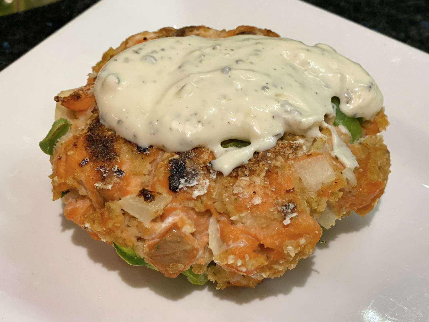 close up view of a Salmon Burger with Lemon Basil Mayo on a white plate