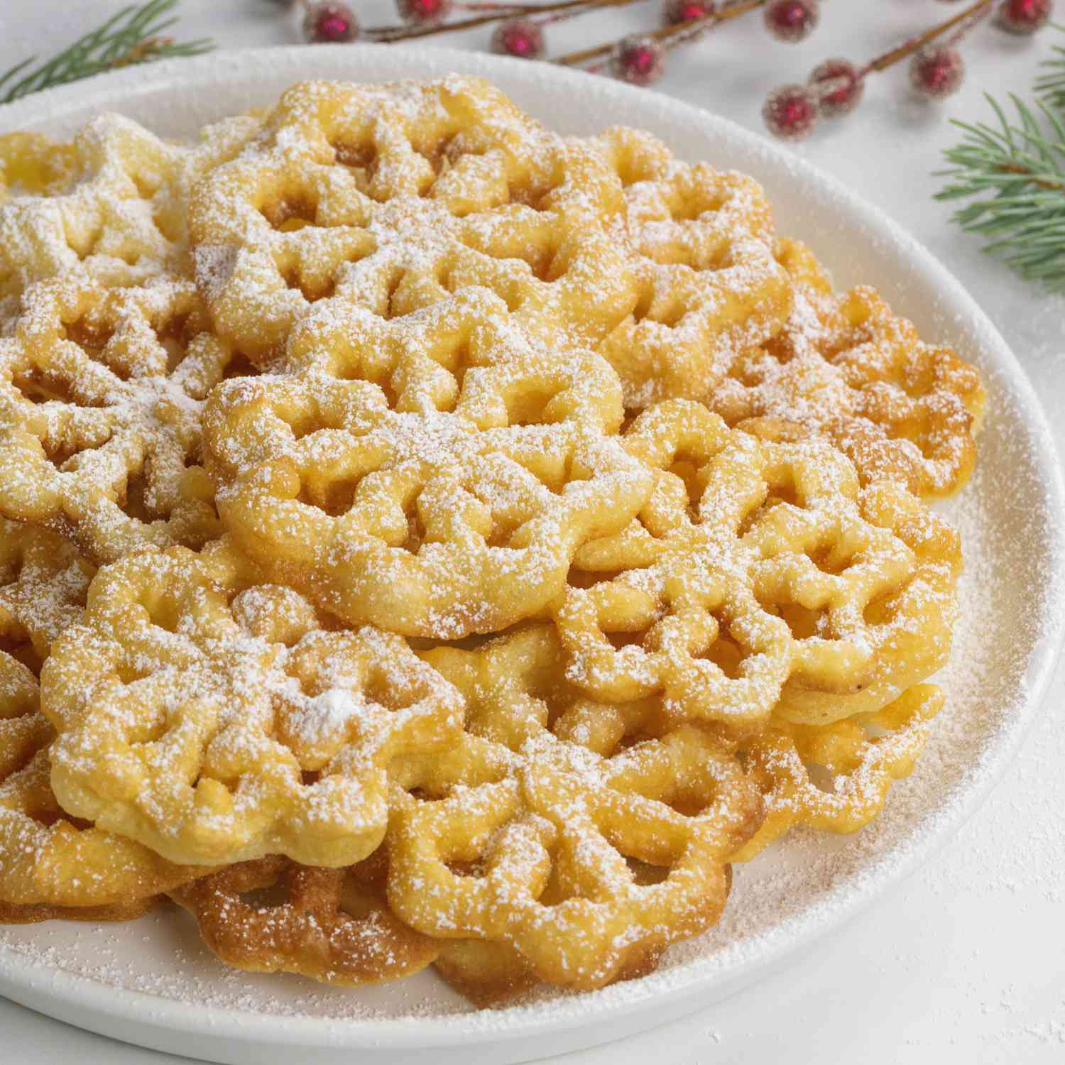 a close up view of a plate full of golden brown rosettes dusted with confectioners sugar