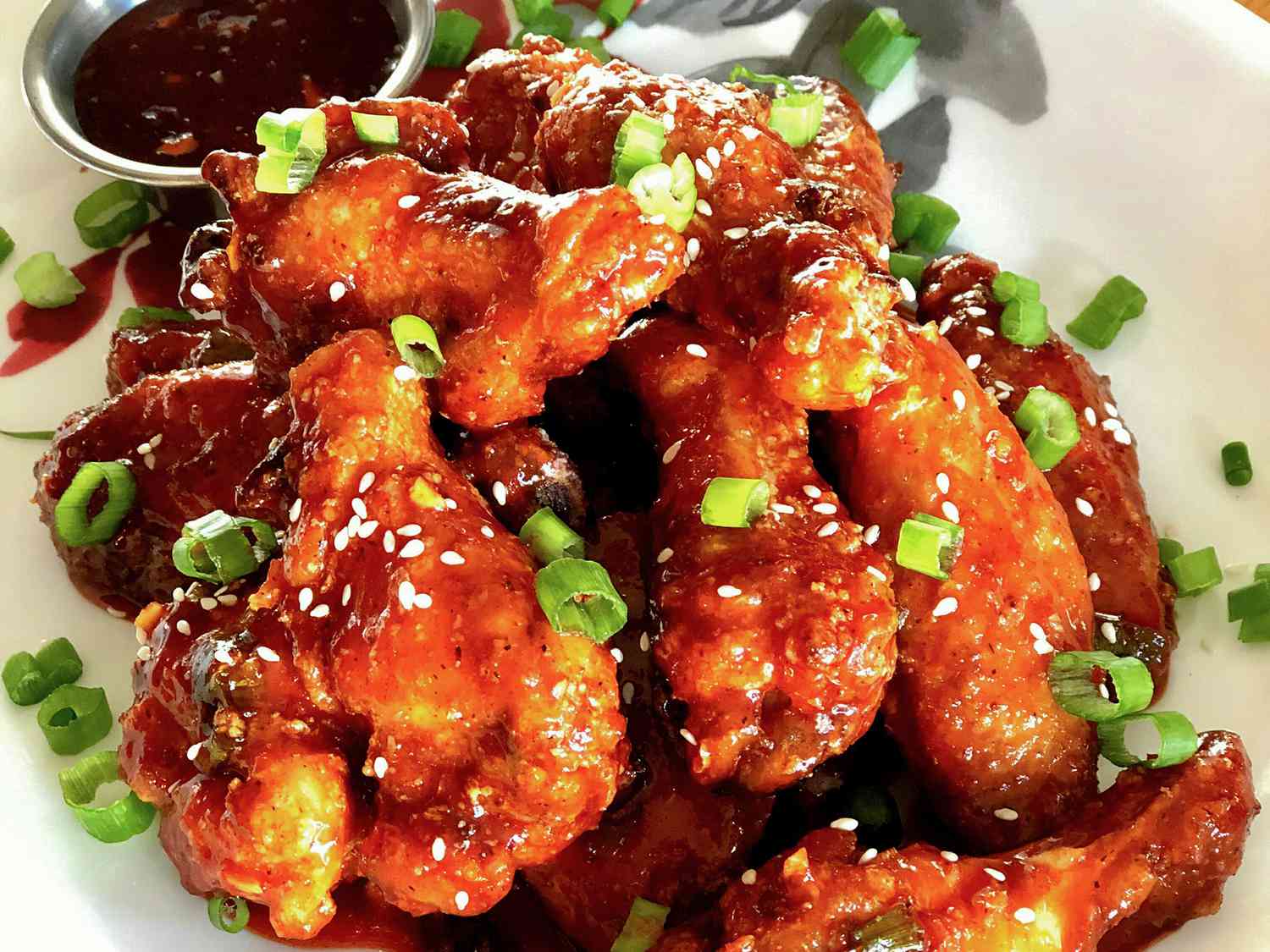 close up view of Korean Chicken Wings garnished with green onions and sesame seeds, with sauce on the side