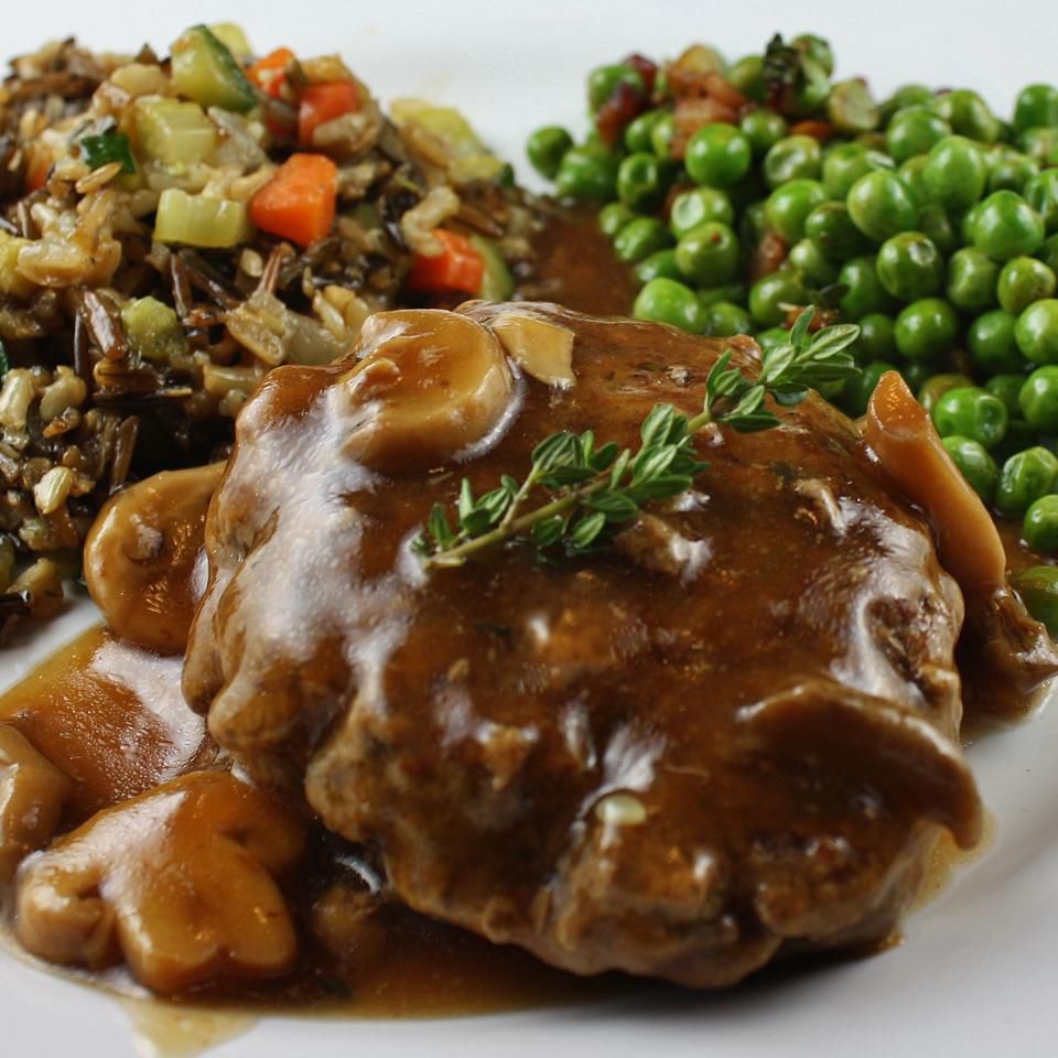 salisbury steak with mushrooms on a white plate with peas and other veggies