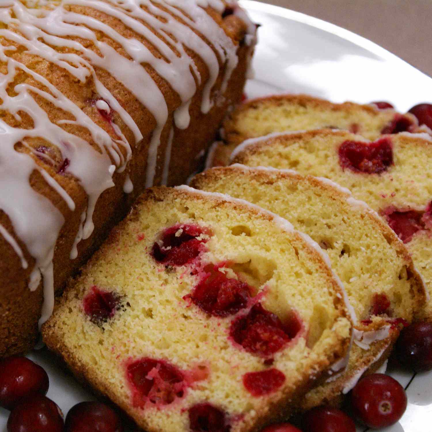 close up view of a sliced Cranberry Orange Loaf on a white platter, garnished with cranberries