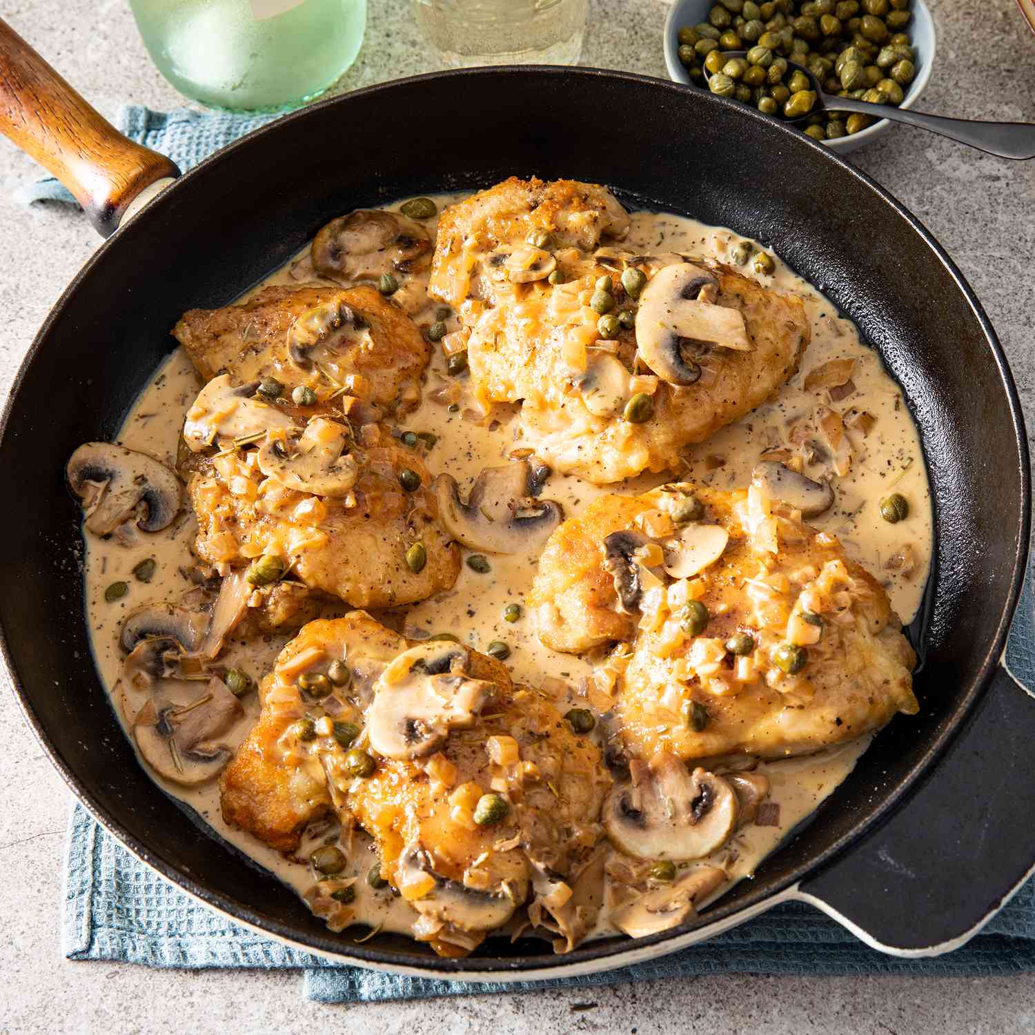 close up view of chicken fillets with mushrooms, sauce and capers in a pan