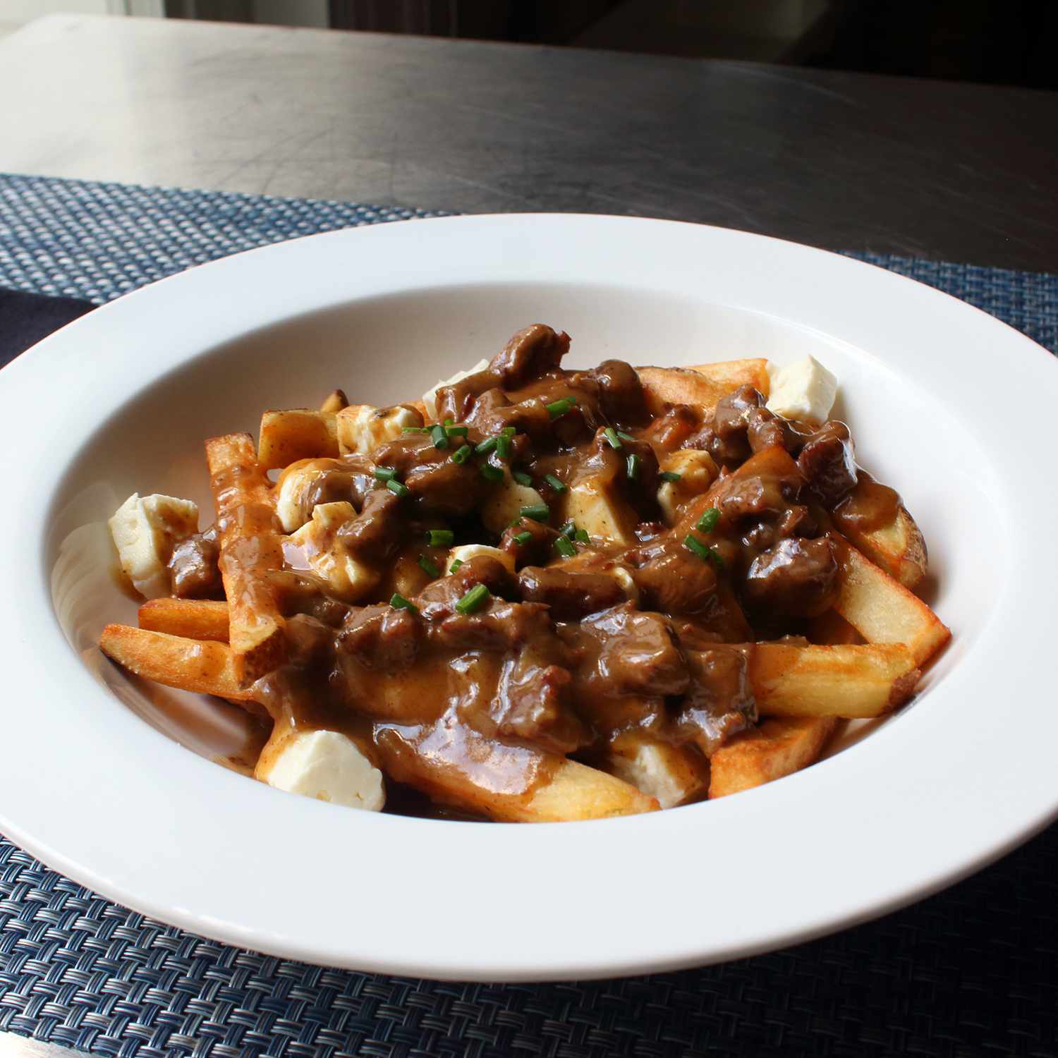 close up view of french fries with cheese, Poutine Gravy and fresh herbs in a white bowl