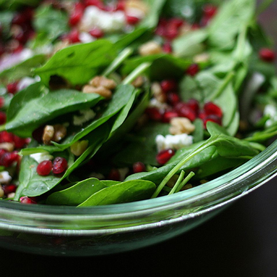 closeup of spinach pomegranate salad in clear bowl