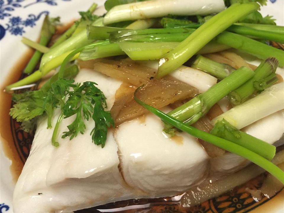 close up view of Steamed Fish with Ginger, green onions, and herbs on a platter