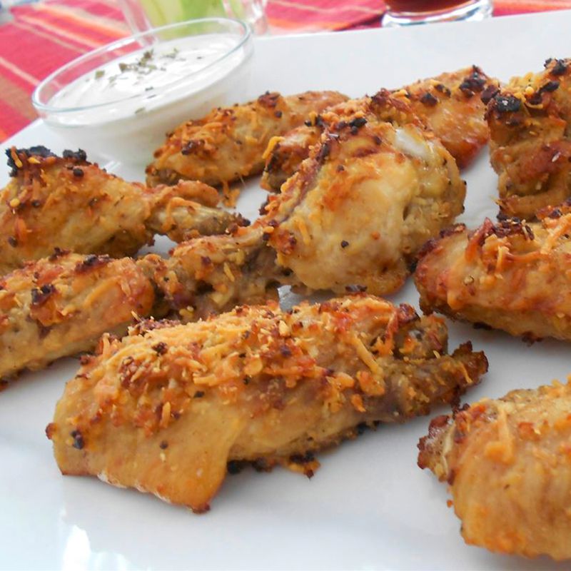 close up view of Garlic and Parmesan Chicken Wings on a white platter, with sauce in a bowl