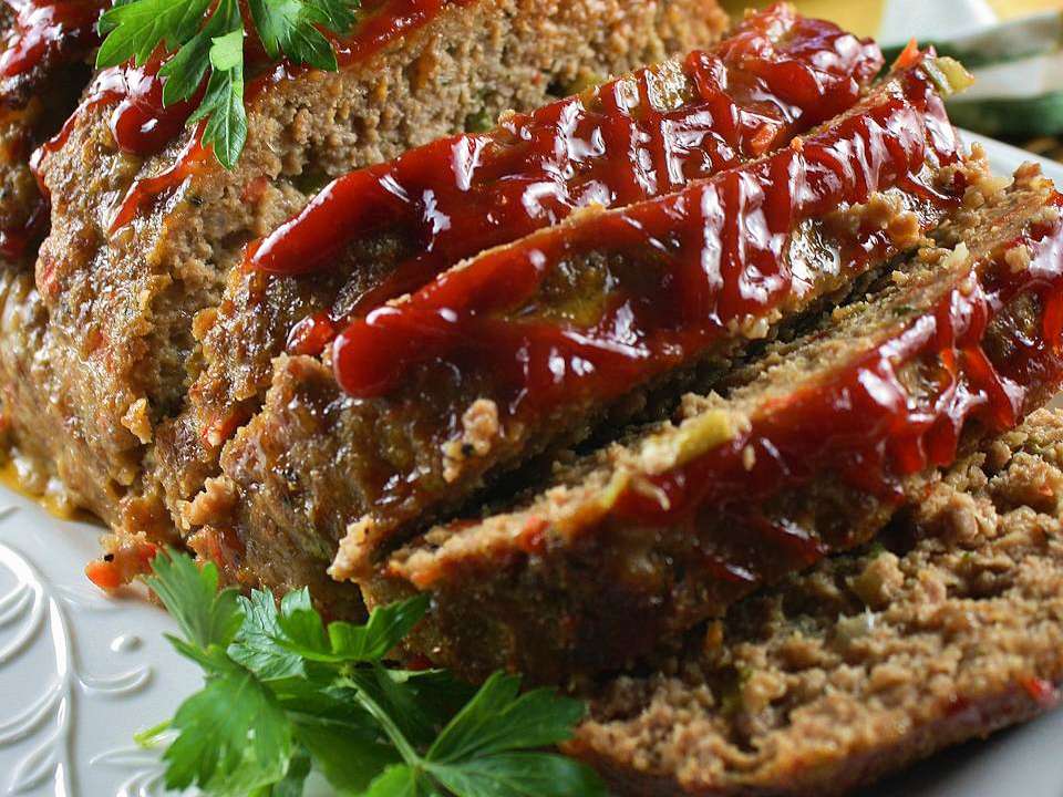 close up view of a sliced Classic Spicy Meatloaf garnished with fresh herbs on a platter