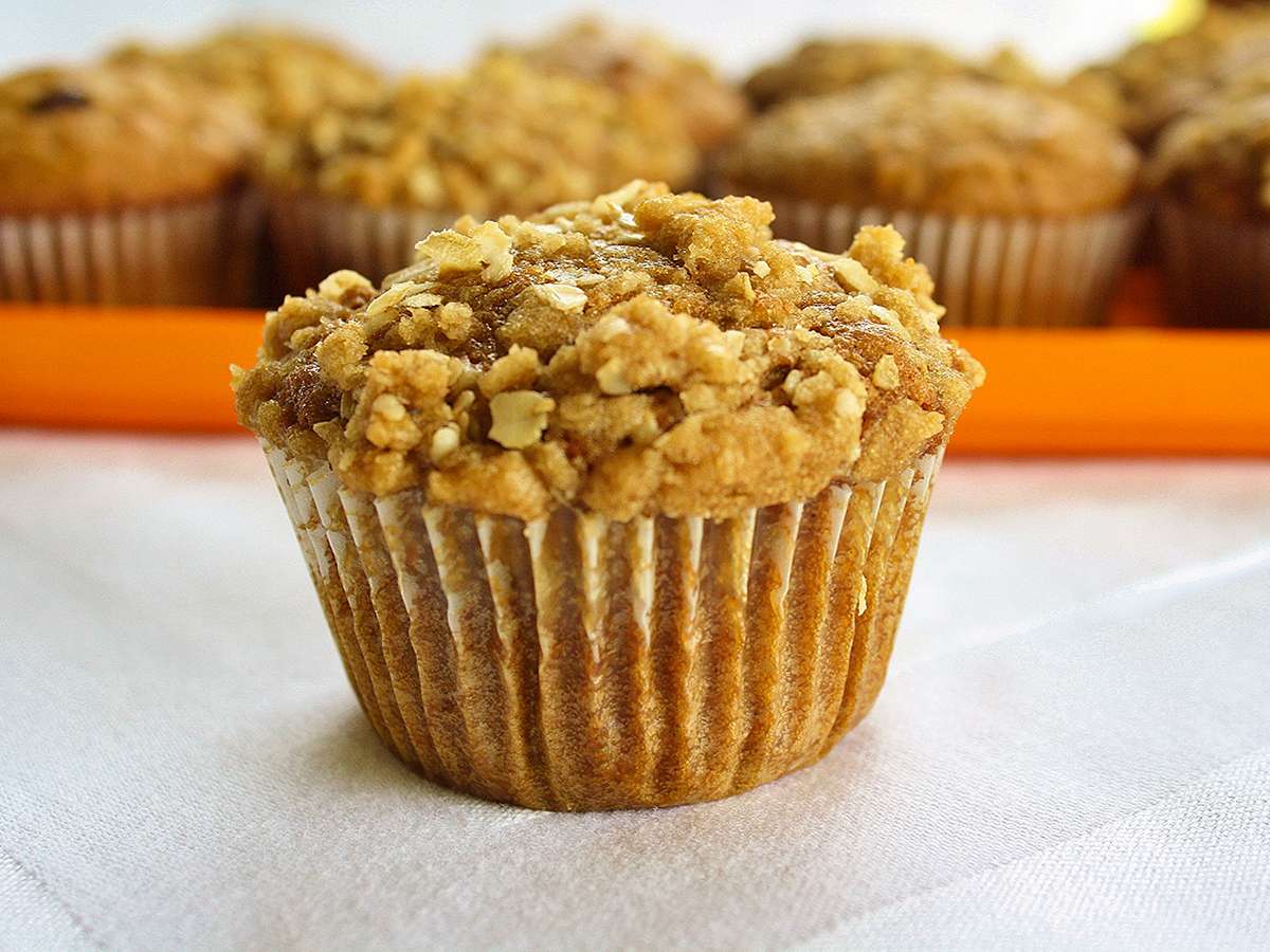 close up view of a Pumpkin Muffin with Streusel Topping, and pumpkin muffins in the background