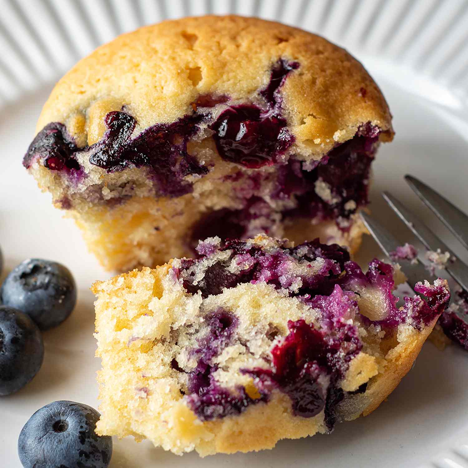 A blueberry muffin broken open with more fresh blueberries on the plate