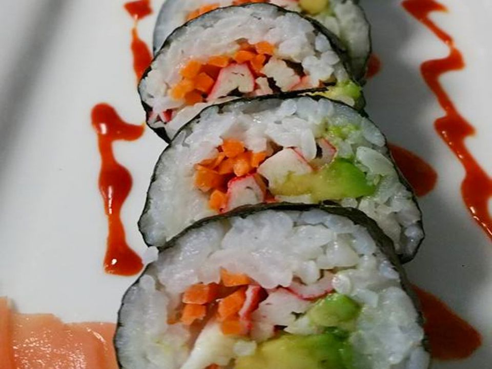 close up view of California Roll Sushi pieces with ginger and sriracha on a white platter