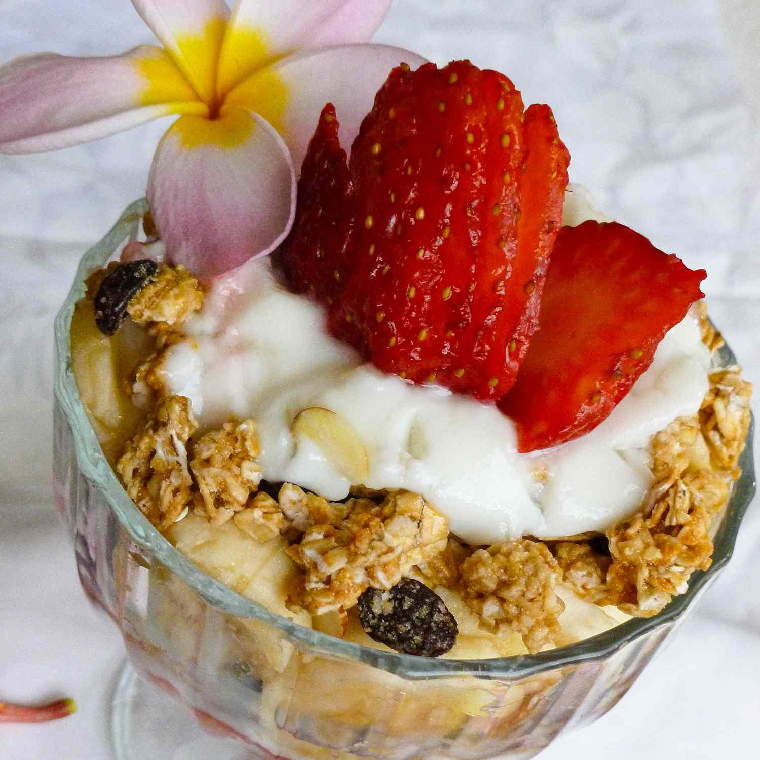 close up view of a Summer Berry Parfait with Yogurt and Granola garnished with a sliced strawberry and a flower in a glass bowl