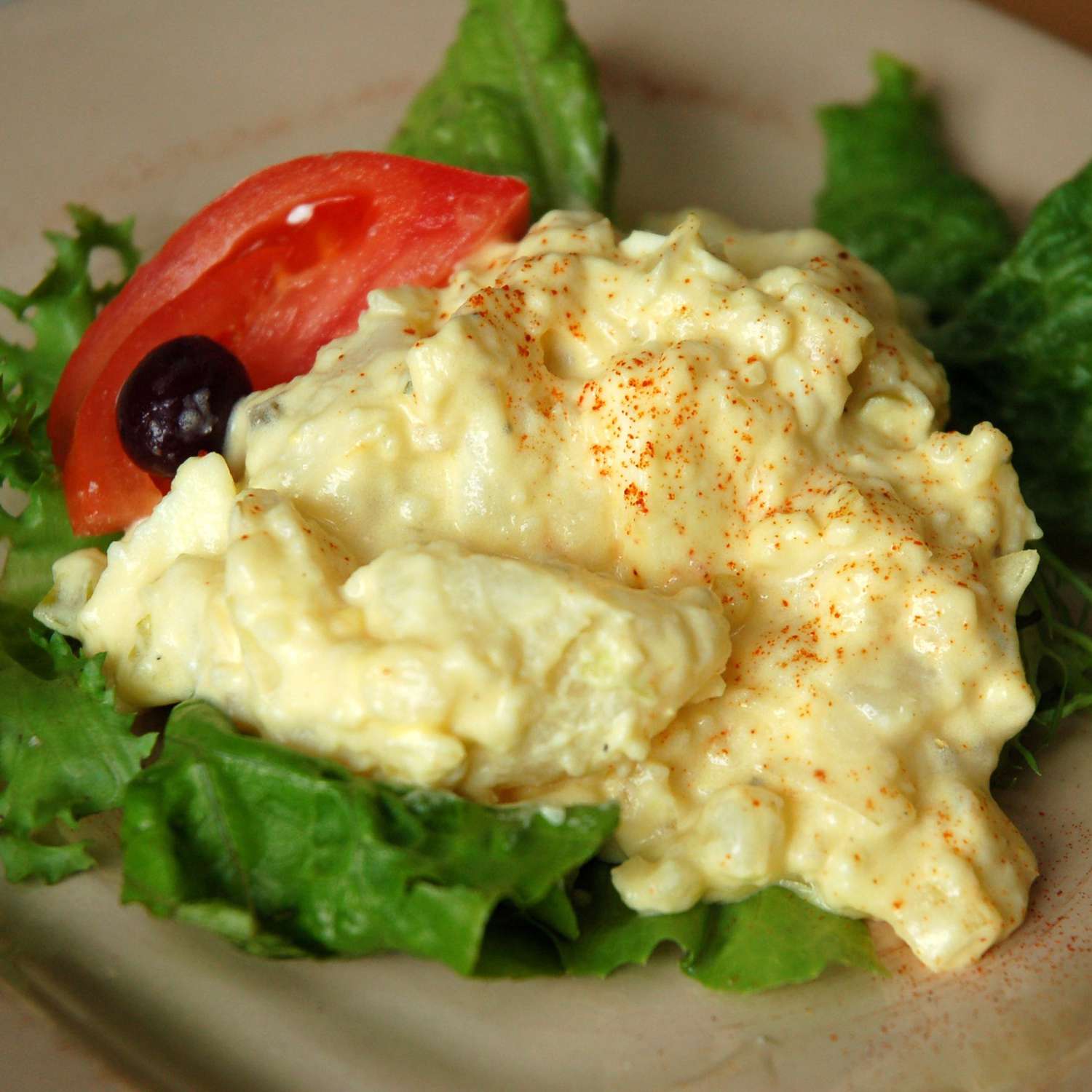 close up view of Potato Salad garnished with lettuce, tomato and a black olive
