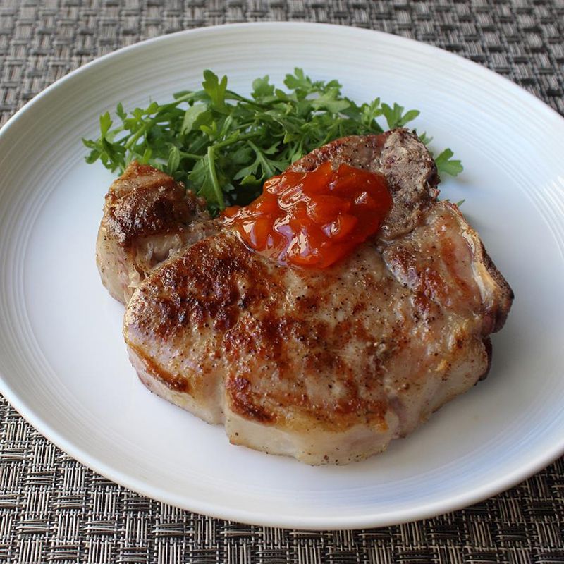 close u p view of cooked pork chops with red sauce and arugula on a white plate
