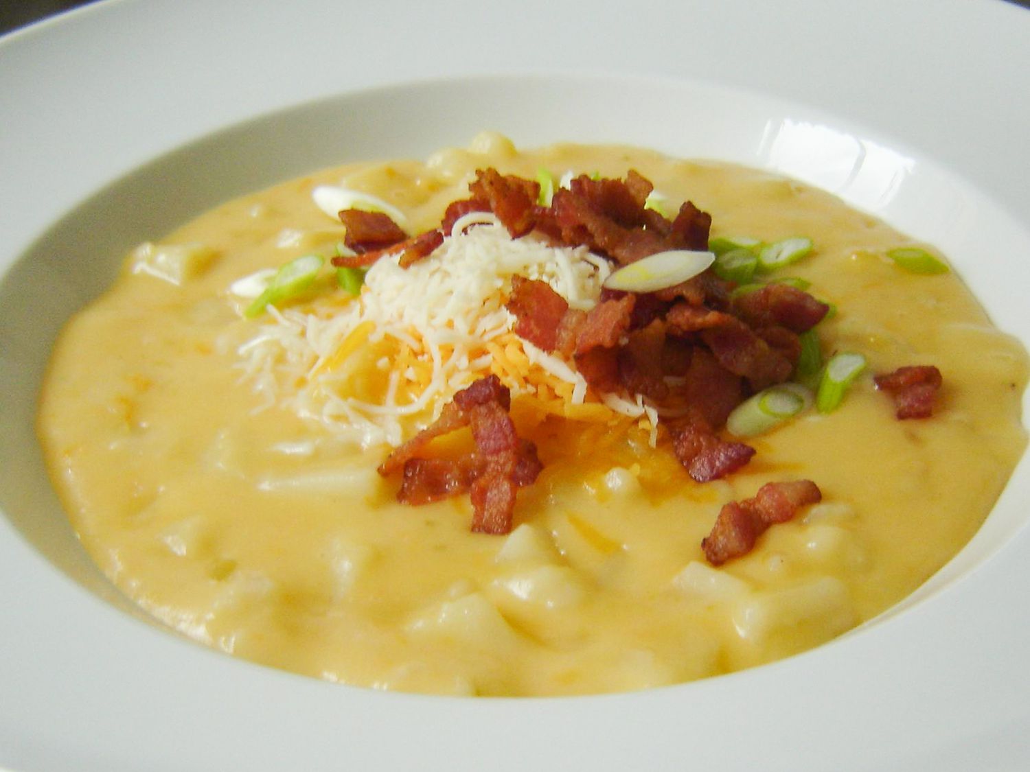 close up view of Potato Cheese Soup garnished with cheese, bacon and green onions in a bowl