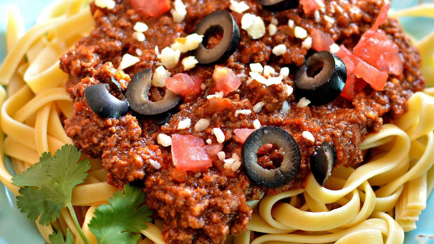 top-down view of linguine topped with a meat sauce with chopped tomatoes, black olives, and parmesan