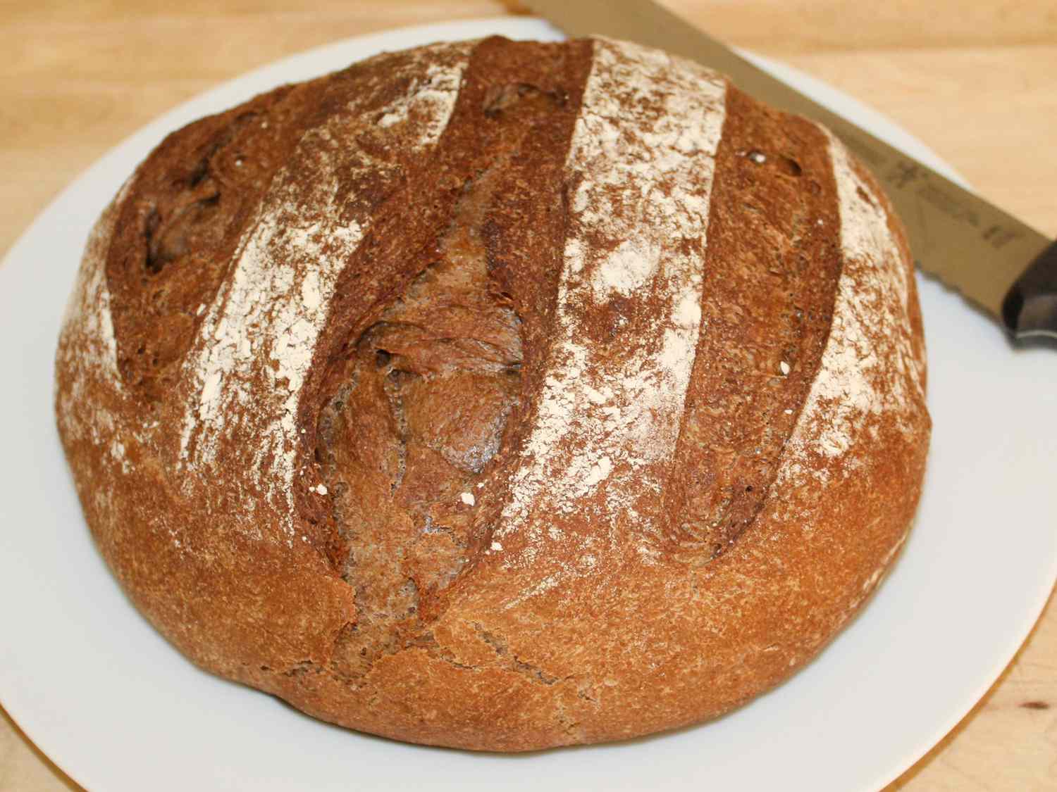 close up view of a loaf of Dark Rye Bread on a white plate with a knife