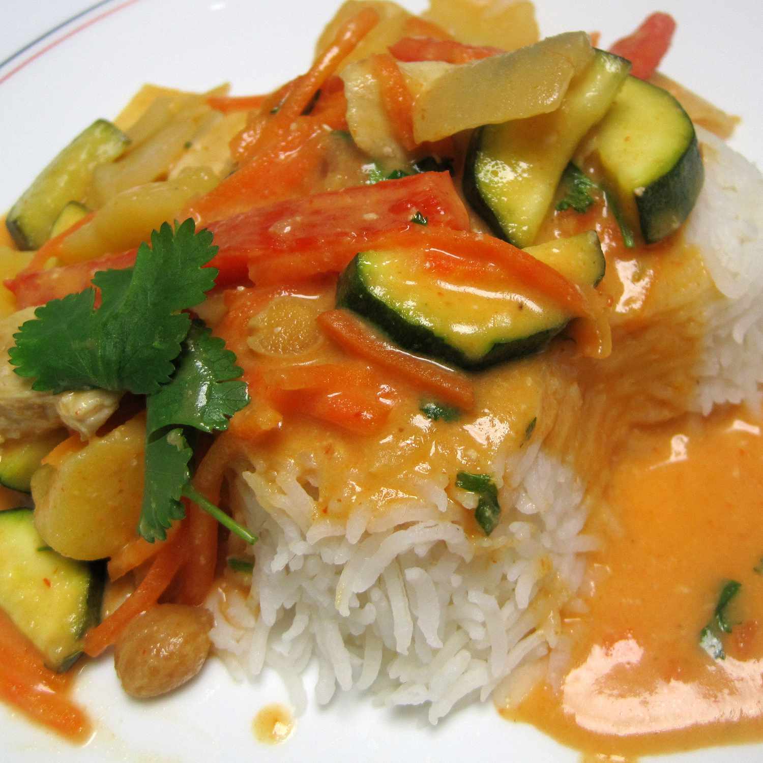 close up view of Thai Red Chicken Curry garnished with fresh herbs over white rice on a white plate