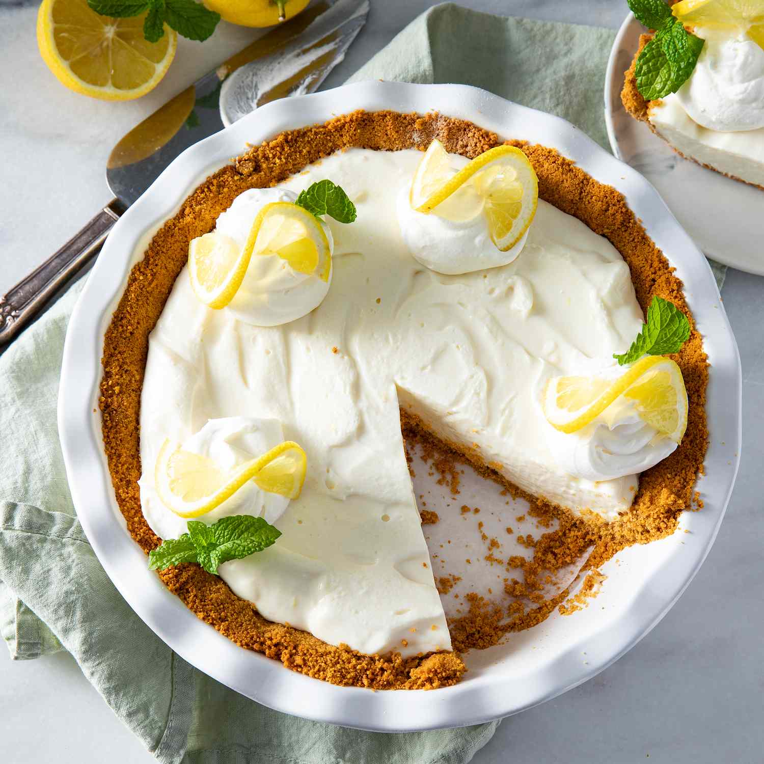 close up view of Lemon Icebox Pie in a white pie pan, garnished with lemon and mint