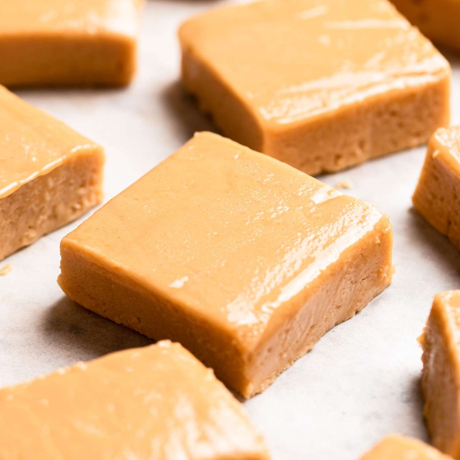 a close up view of cut squares of creamy peanut butter fudge resting on a piece of parchment paper