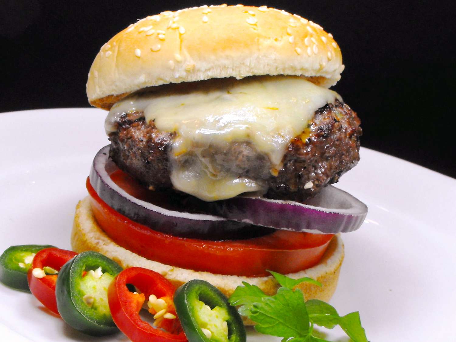 close up view of Jalapeno-Garlic-Onion Cheeseburger with peppers on a white plate