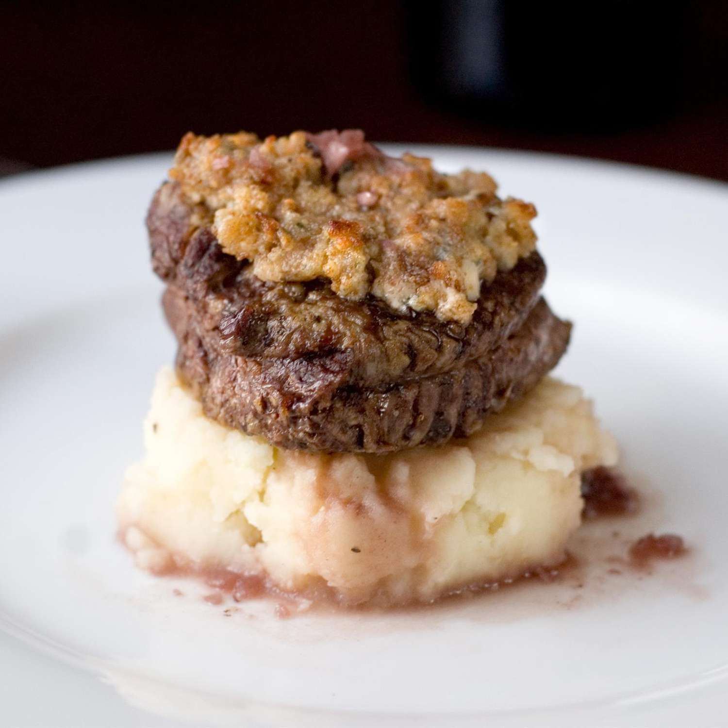 close up view of Blue Cheese Crusted Filet Mignon with Port Wine Sauce on top of mashed potatoes on a white plate