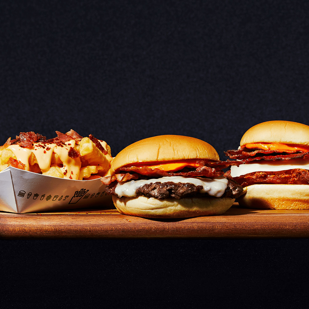 The three items in the Shake Shack Hot Ones collaboration sit on a black background: spicy cheese fries, spicy chicken sandwich, and a spicy shack bacon cheeseburger.
