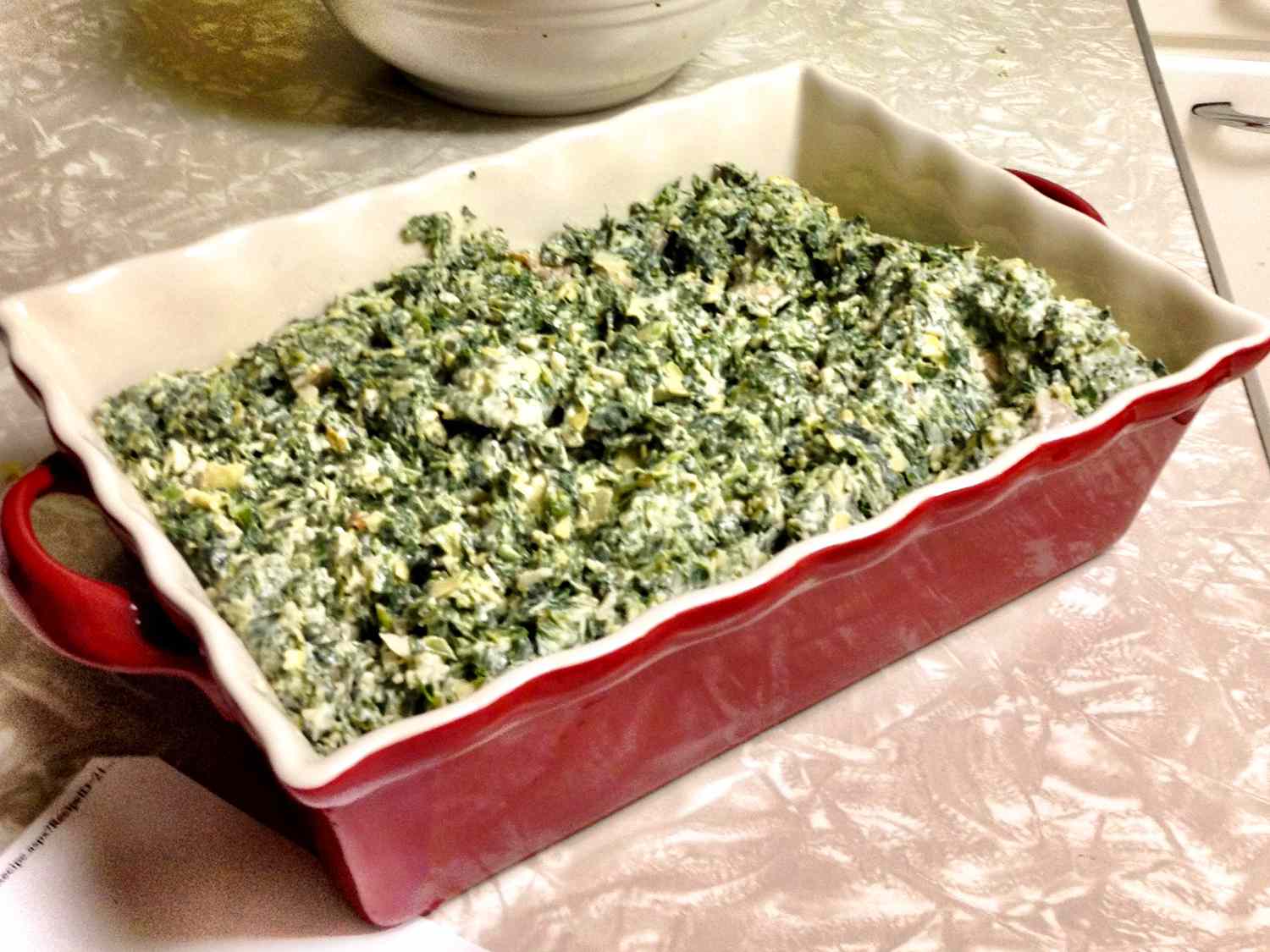 close up view of Spinach Artichoke Casserole in a red and white baking dish
