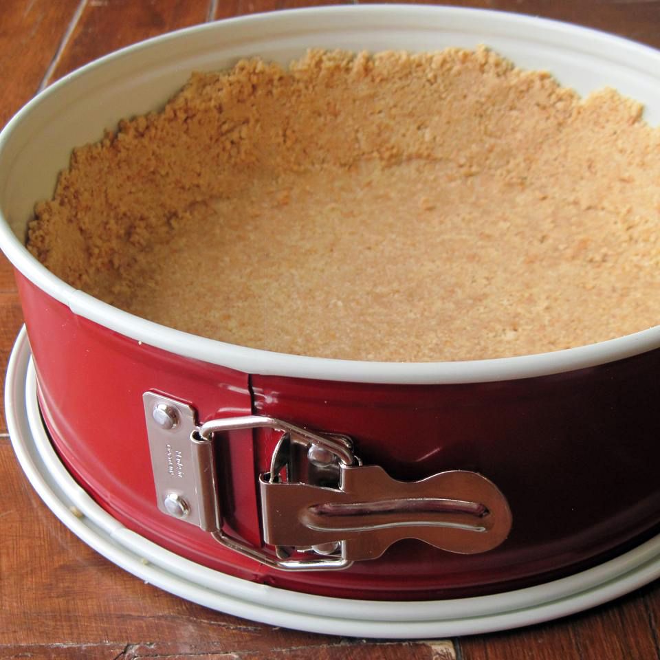 a red springform pan filled with graham cracker crumb crust