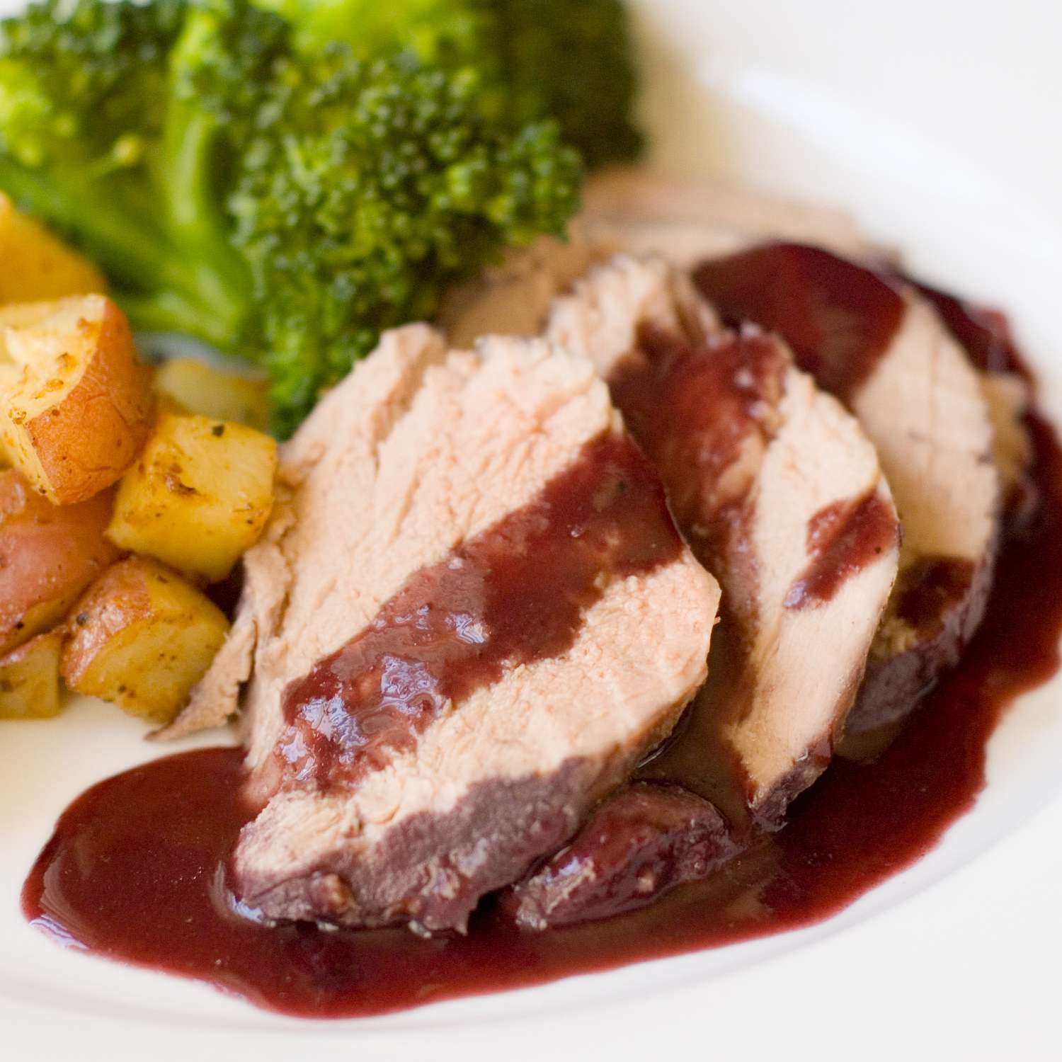 close up view of Burgundy Pork Tenderloin with sauce, served with broccoli and potatoes on a white plate