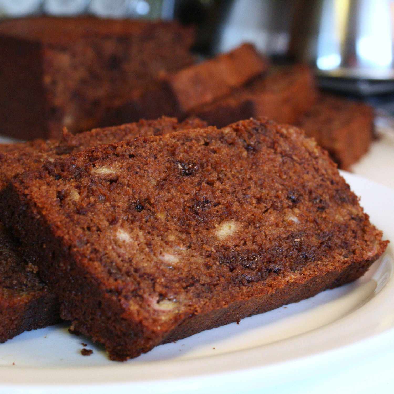 close up view of slices of dark brown banana bread made with cocoa powder and chocolate chips on a white platter