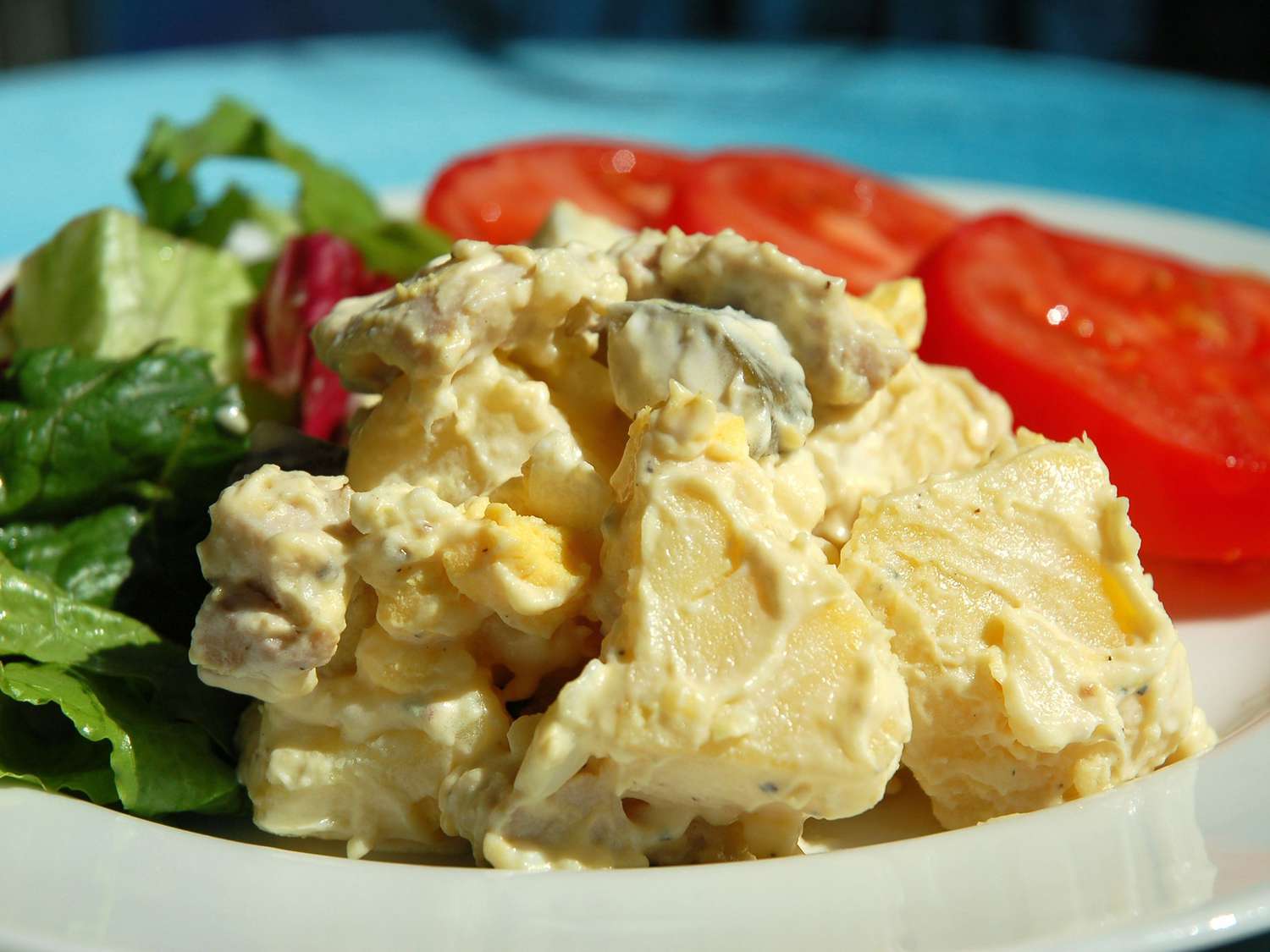 close up view of Chicken Potato Salad on a plate with lettuce and sliced tomato on a white plate