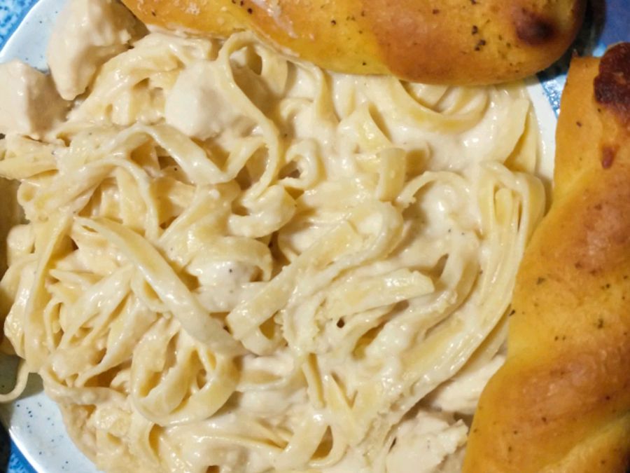 close up view of Chicken Alfredo pasta with bread rolls in a bowl