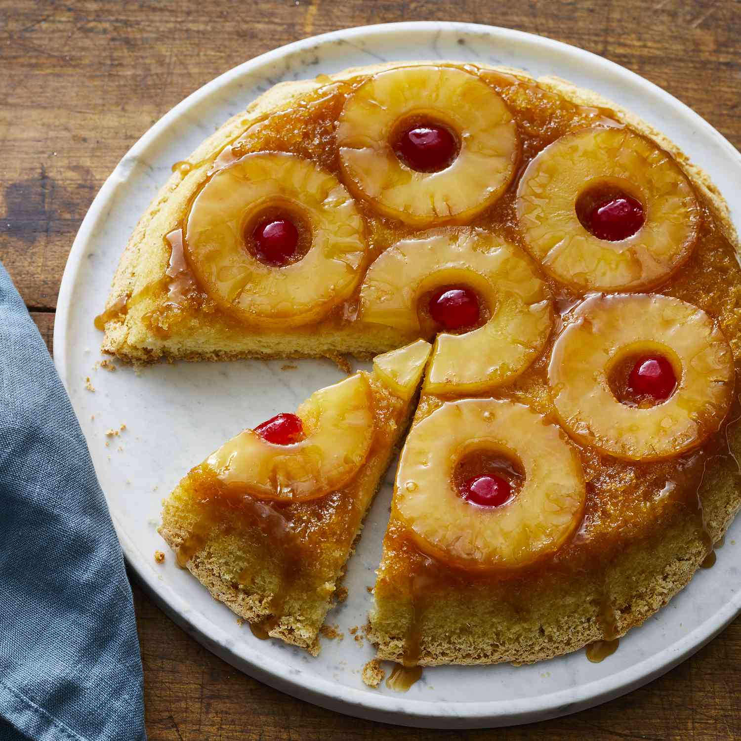 high angle, looking at a pineapple upside down cake on a platter, with a slice cut