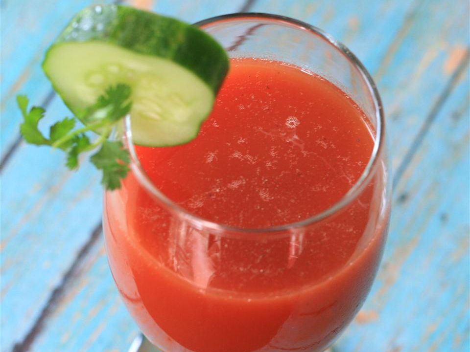 close up view of a Tomato Juice Cocktail garnished with a slice of cucumber and fresh herbs in a glass